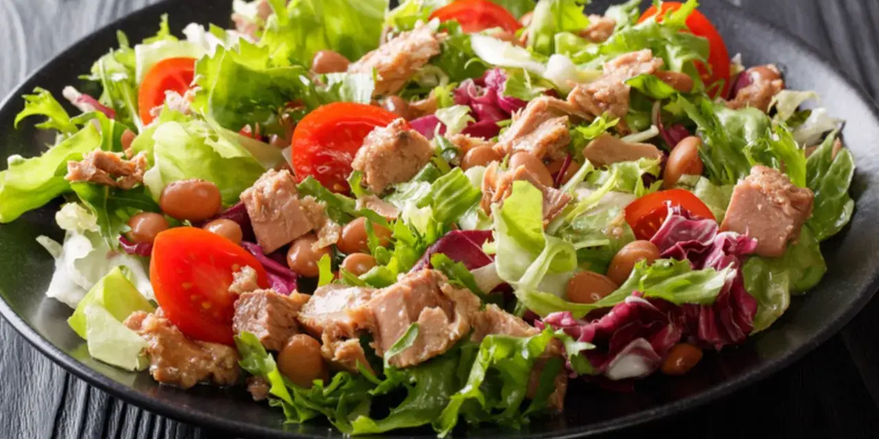 Ein frischer Thunfischsalat mit knackigem Salat, Tomaten und Bohnen auf einem schwarzen Teller.