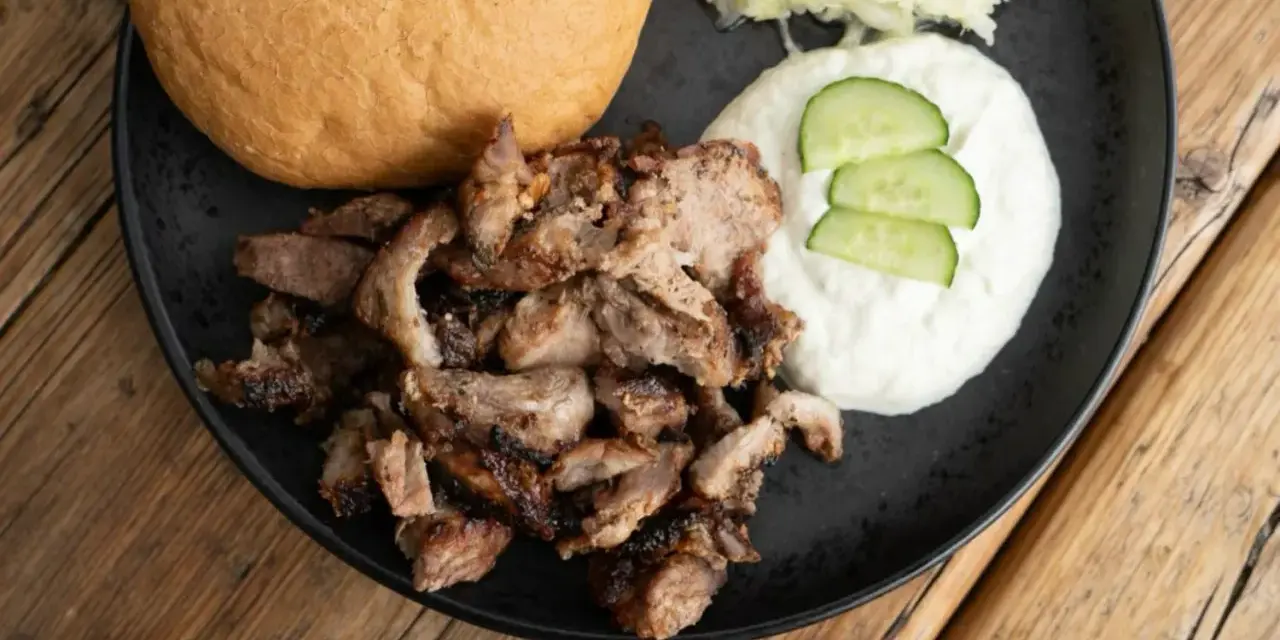 Ein Teller mit gegrilltem Fleisch, einem Brötchen, Tzatziki und Krautsalat. Perfekt für ein leckeres Gyros Rezept.
