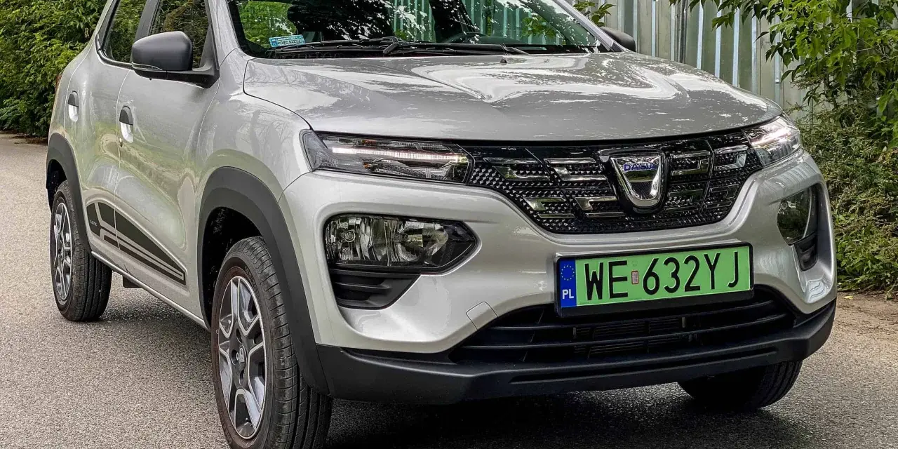Srebrna Dacia Spring z zieloną tablicą rejestracyjną WE 632YJ, przód samochodu.