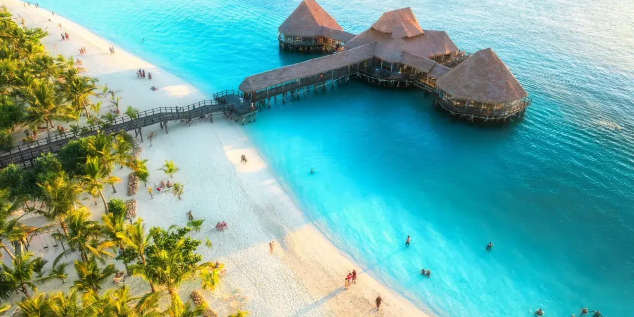 Rajska plaża na Zanzibarze z palmami i restauracją na wodzie. Sprawdź Zanzibar ceny, by zaplanować wymarzone wakacje.