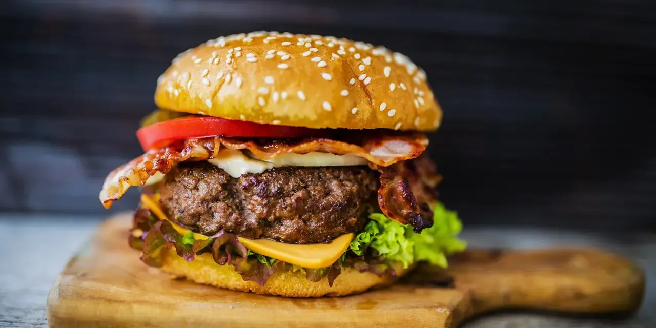 Soczysty burger z bekonem, serem i warzywami na desce.