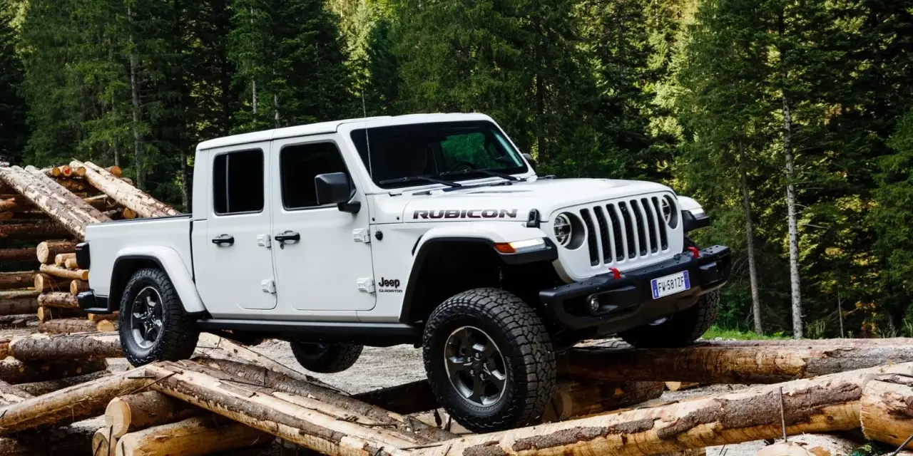 Biały jeep pickup Rubicon pokonuje przeszkodę z bali drewna w lesie.