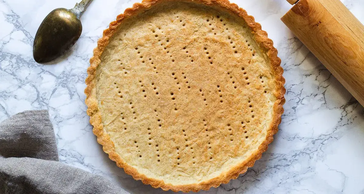 En gyllene pajskal, perfekt för ditt pajdeg recept. En kavel och en gammal sked ligger bredvid.