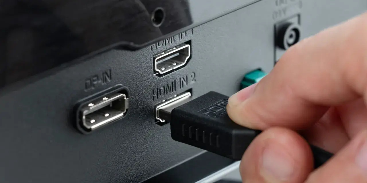 Hand steckt HDMI-Kabel ein, um den PC mit dem Fernseher zu verbinden. Anschlüsse für DisplayPort und HDMI sind sichtbar.