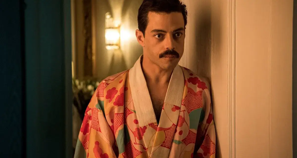 Freddie Mercury w barwnym szlafroku, jakby zrodzony z **bohemian rhapsody**, opiera się o drzwi.