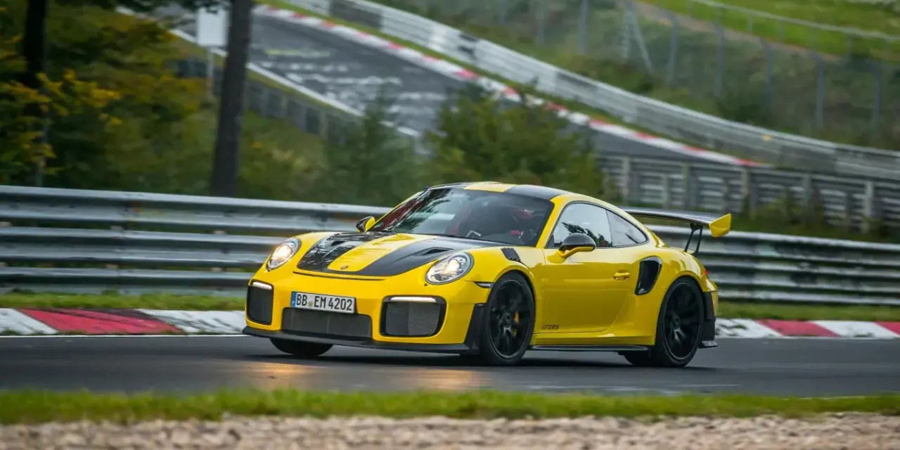 Żółty Porsche 911 GT2 RS z czarnymi pasami pędzi po torze wyścigowym.