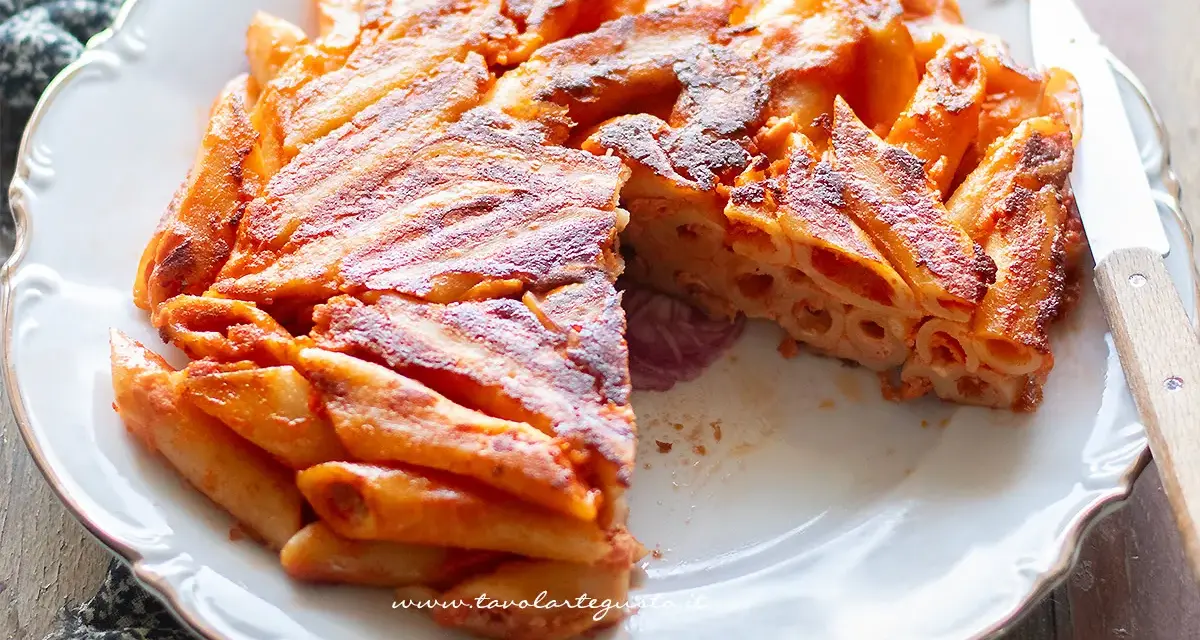 Una deliziosa frittata di pasta, dorata e croccante, servita su un piatto bianco con un coltello.