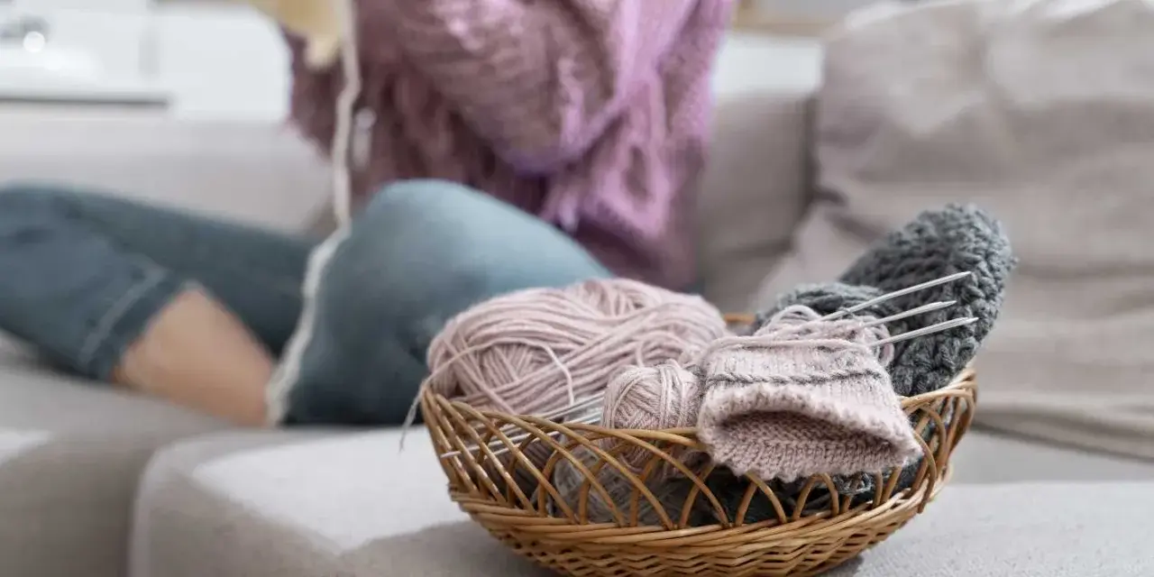 Koszyk z włóczką i drutami. Czy farba do tkanin się spiera? Kobieta w swetrze dzierga na drutach.