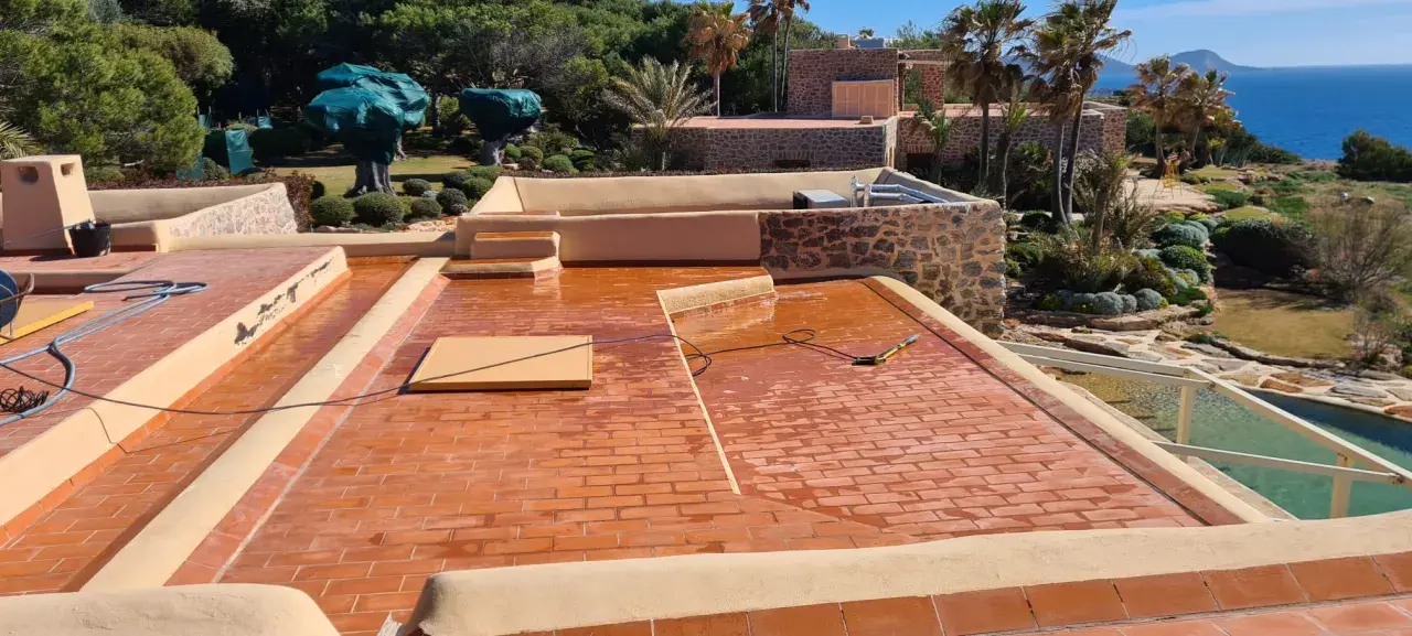 Proceso de impermeabilizar terraza con acabado de tejas rojas. El sol brilla sobre la superficie mojada, lista para proteger la casa.