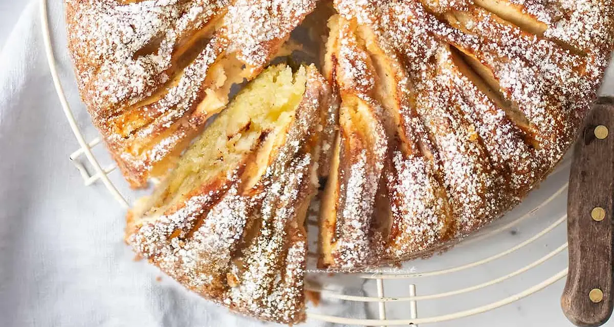 Deliziosa torta di mele in friggitrice ad aria, cosparsa di zucchero a velo, con una fetta tagliata che mostra la morbidezza dell'interno.