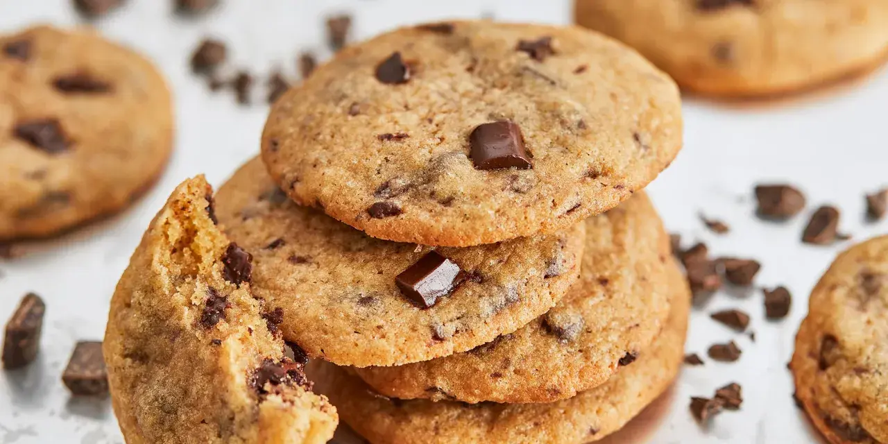 Ein Stapel saftiger american cookies mit Schokoladenstückchen, einer angeknabbert, umgeben von Schokoladenstückchen.
