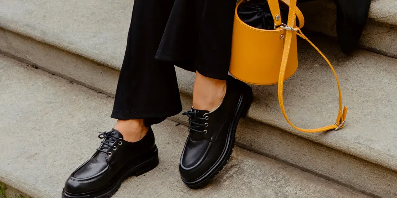 Come abbinare le stringate femminili: look audace con pantaloni neri e borsa gialla.
