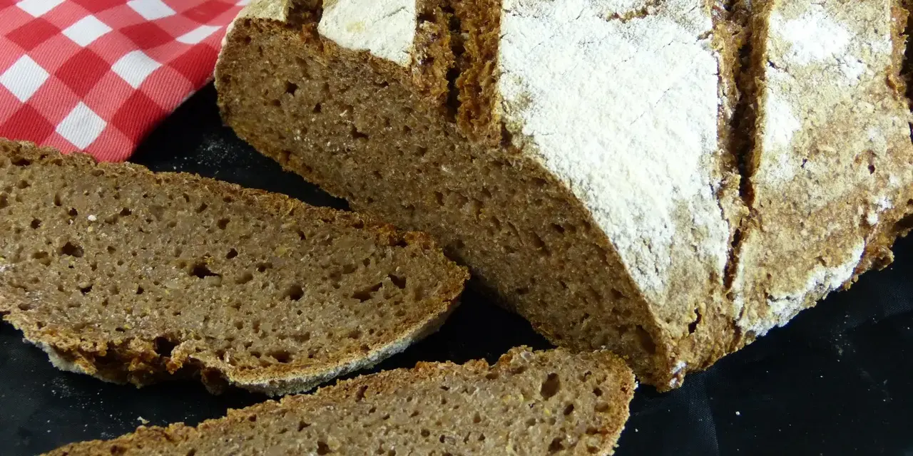 Ein rustikales tschechisches Brot, frisch aufgeschnitten, mit einer kräftigen Kruste und einer saftigen Krume. Daneben liegt eine rot-weiß karierte Serviette.