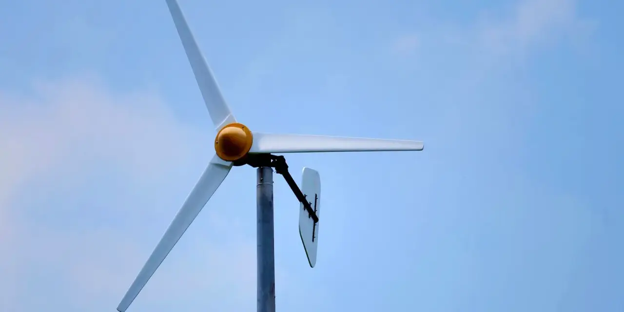 Biała elektrownia wiatrowa z żółtym elementem na środku, na tle błękitnego nieba z chmurami.