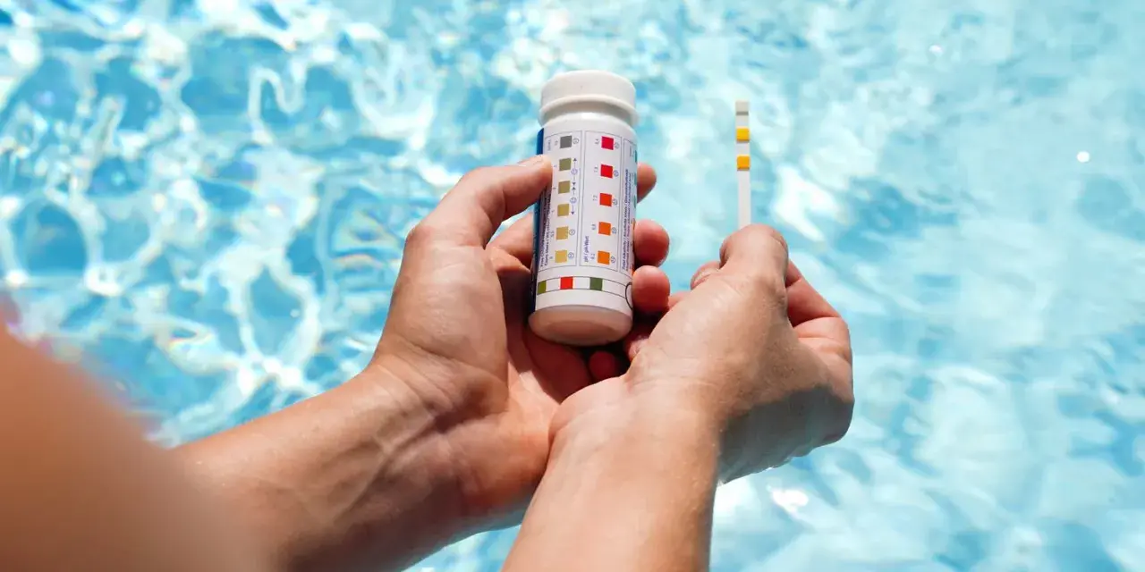 Hands hold a pool test strip and bottle, showing how to make pool water clear by checking chemical levels.