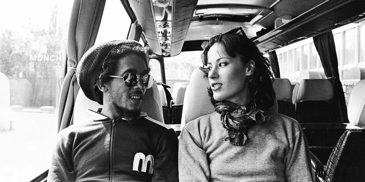 Bob Marley i Kate Marley w autobusie, patrzą na siebie z uśmiechem.