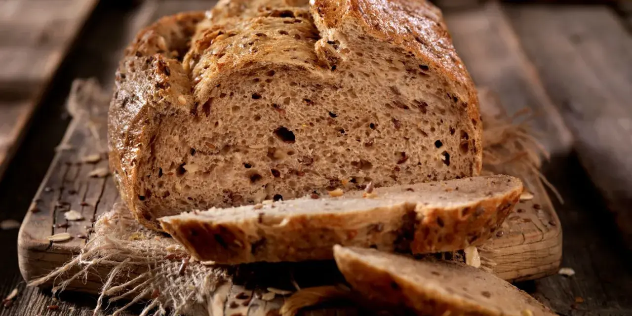 Frisch gebackenes Körnerbrot, angeschnitten auf einem Holzbrett. Perfekt, wann Brot aus der Form nehmen, um diese Kruste zu erhalten.