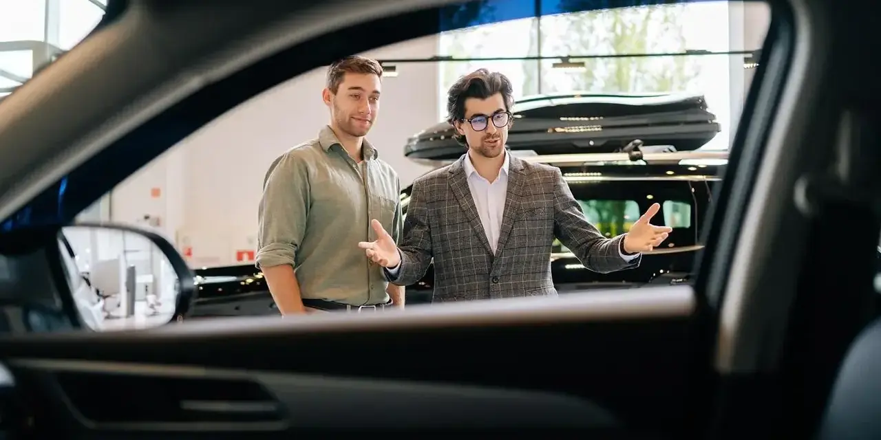 Dwóch mężczyzn w salonie samochodowym, jeden prezentuje auto.