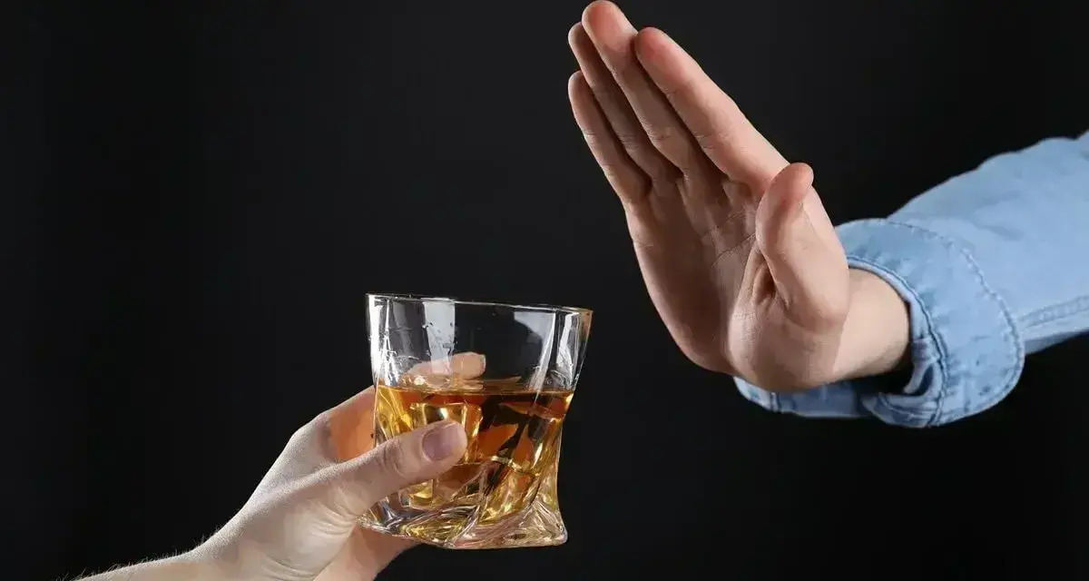 Dłoń odrzuca szklankę z bursztynowym płynem. Pytanie: czy po znieczuleniu u dentysty można pić alkohol?