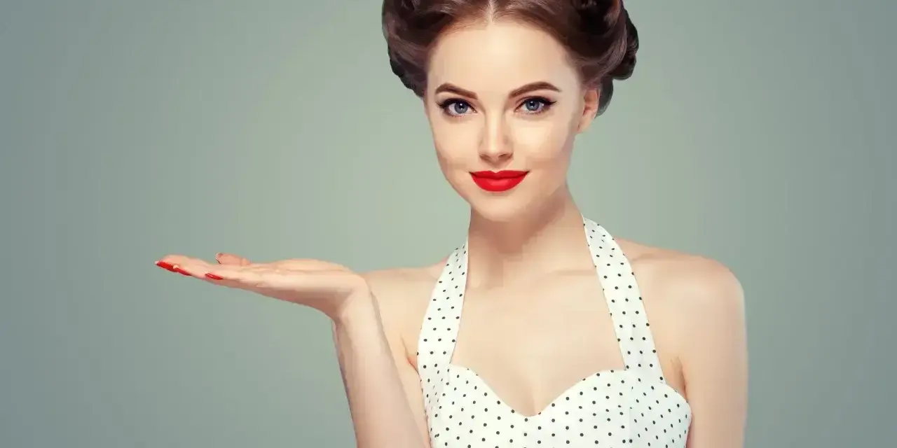 Uśmiechnięta pin-up girl w grochy, z burzą loków i czerwoną szminką, prezentuje coś na otwartej dłoni.