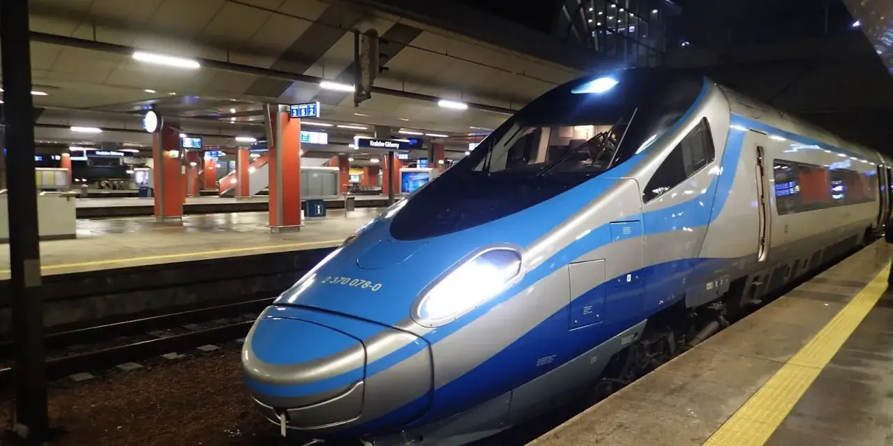 Nowoczesny pociąg Pendolino na peronie. Jego niebiesko-srebrne malowanie i ostre linie zapowiadają szybką podróż.