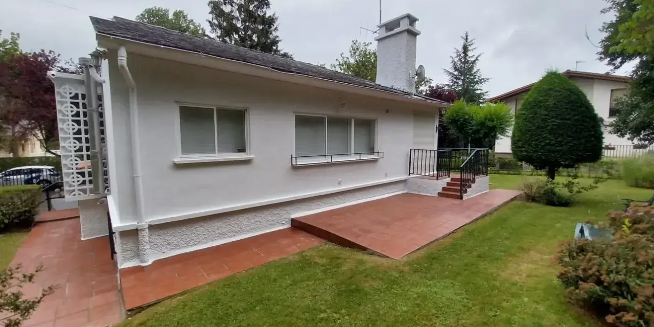 Terraza exterior con suelo de baldosas rojas recién pintado, rodeada de césped verde y un jardín frondoso.