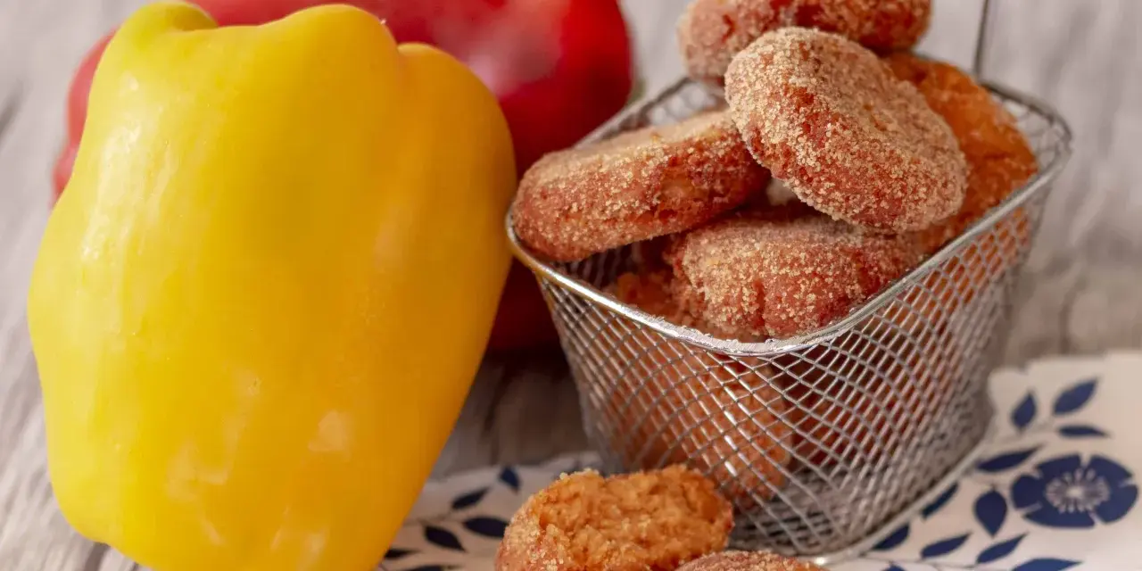 Polpette di peperoni dorate e croccanti, servite in un cestino, accanto a peperoni freschi rossi e gialli.