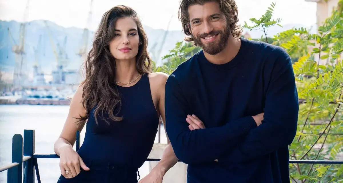 Coppia sorridente con sfondo di un porto, il suo sguardo è viola come il mare.