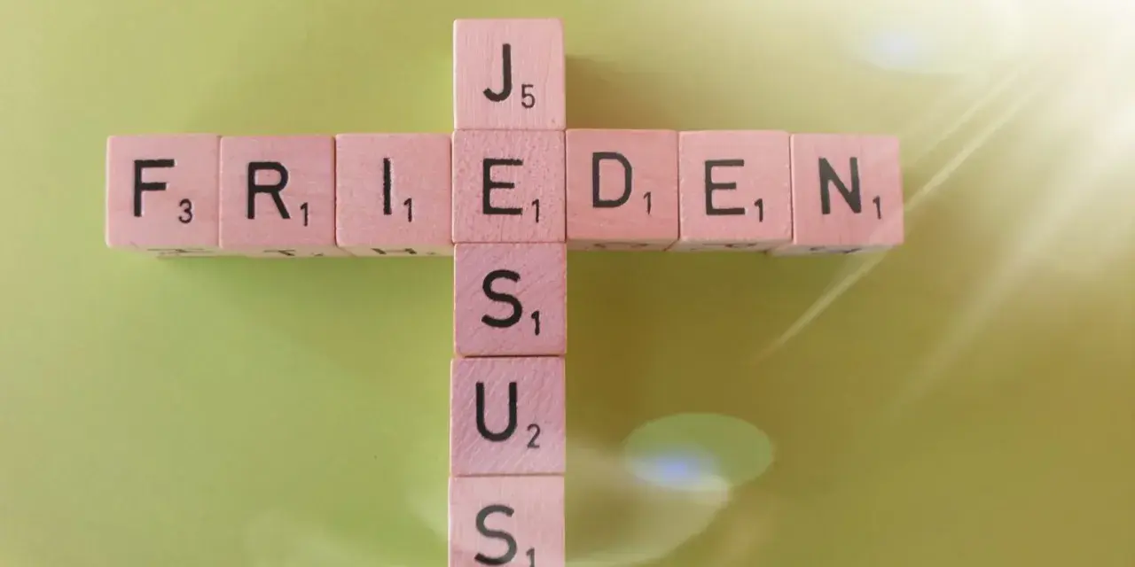 Buchstabensteine bilden ein Kreuz mit den Wörtern "FRIEDEN" und "JESUS". Ein Zitat aus Johannes 14.