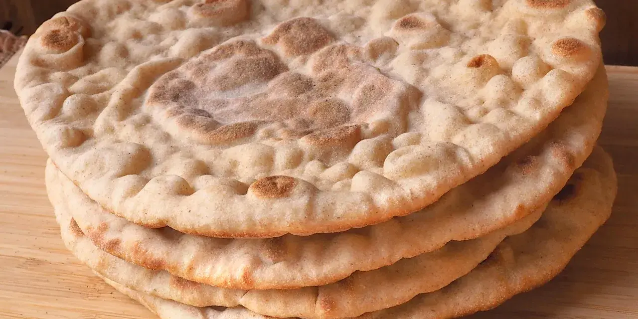 Una pila di pane naan senza lievito, dorato e soffice, su un tagliere di legno.
