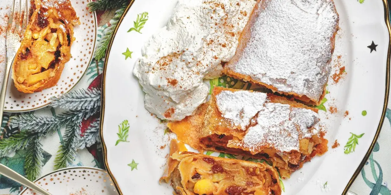 Delizioso strudel di mele con pasta sfoglia, cosparso di zucchero a velo e servito con panna montata e cannella.