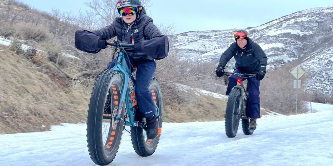 Two people ride fat tire bikes on a snowy path, demonstrating what are fat tire bikes for: tackling challenging winter terrain with their wide tires.