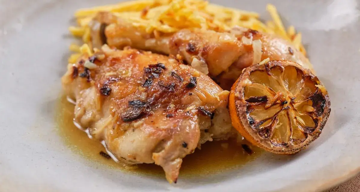 Delicioso pollo al limón con papas fritas crujientes y una rodaja de limón caramelizada.