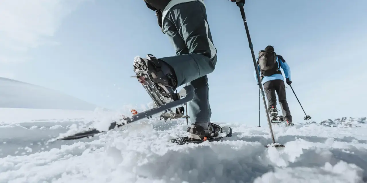 Deux personnes font une randonnée hivernale en raquettes sur un paysage enneigé sous un ciel bleu clair.