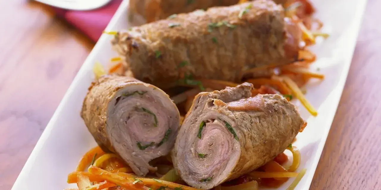 Drei köstliche kalbsrouladen italienisch auf einem Bett aus Gemüse. Eines ist aufgeschnitten und zeigt die saftige Füllung.