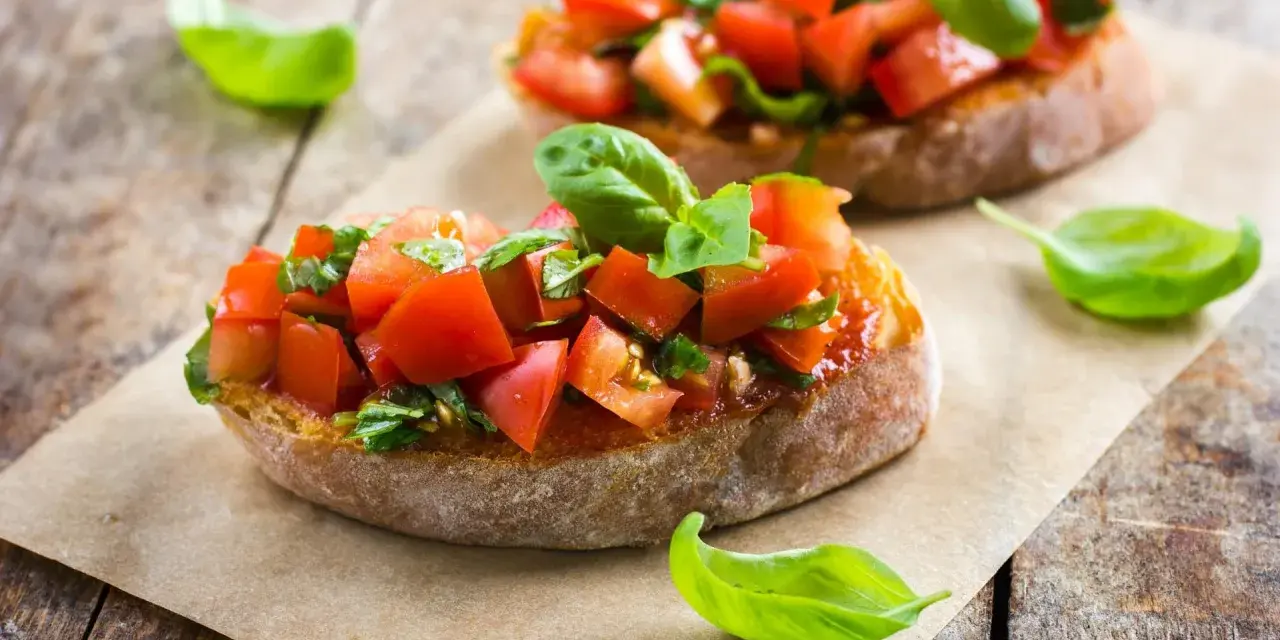 Zwei Bruschetta mit frischen Tomaten und Basilikum, garniert mit einem Hauch von Paprika, auf rustikalem Holz.