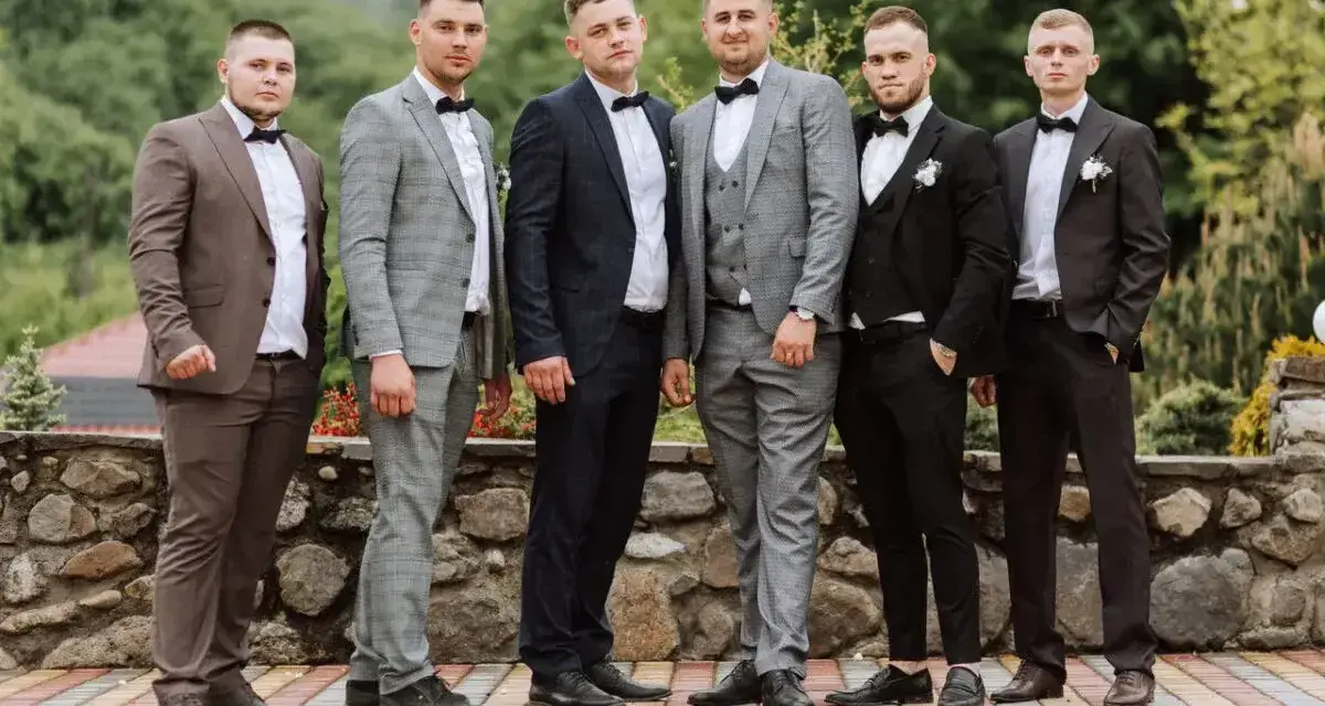 Sześciu mężczyzn w garniturach i białych koszulach, każdy z muszką. Różne kolory i wzory garniturów pokazują, jaka koszula do garnituru pasuje najlepiej.