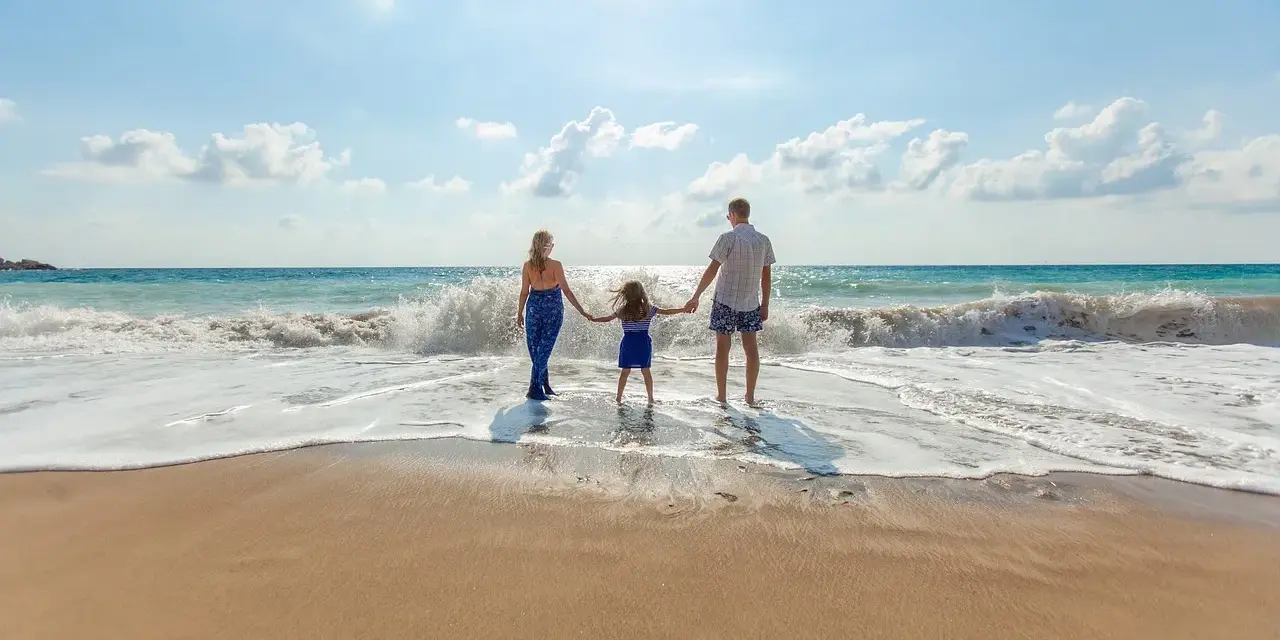Une famille se tient la main sur la plage, profitant des vagues. Ils pensent à devenir famille d'accueil pour les vacances, offrant ces moments de bonheur.