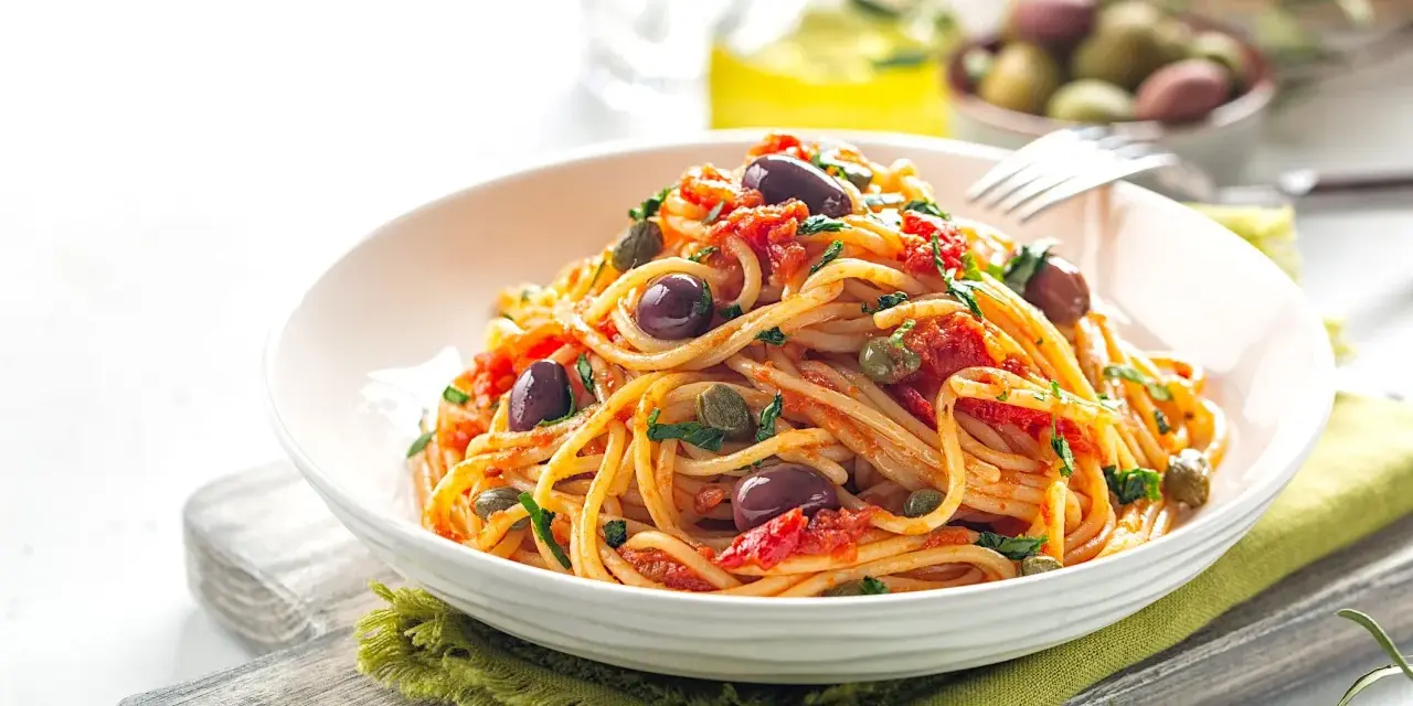 Un piatto invitante di spaghetti alla puttanesca, con olive nere, capperi e pomodoro, pronto per essere gustato.