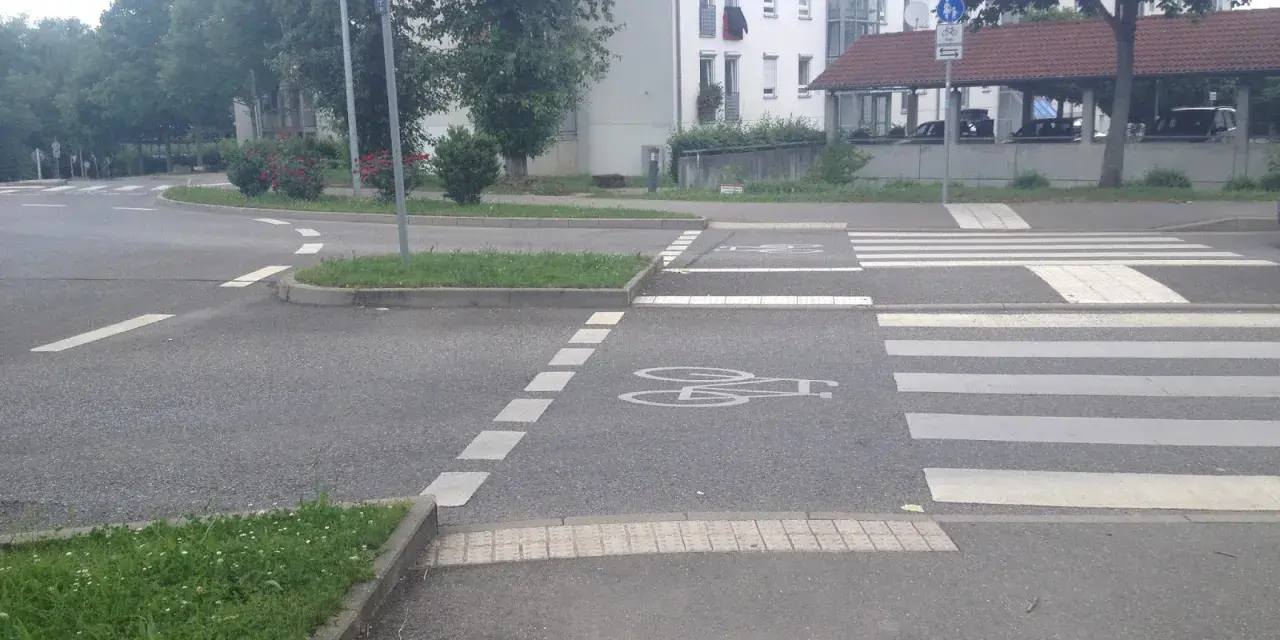 Ein Zebrastreifen mit Fahrradsymbolen auf dem Asphalt. Ein Schild weist in alle Richtungen.