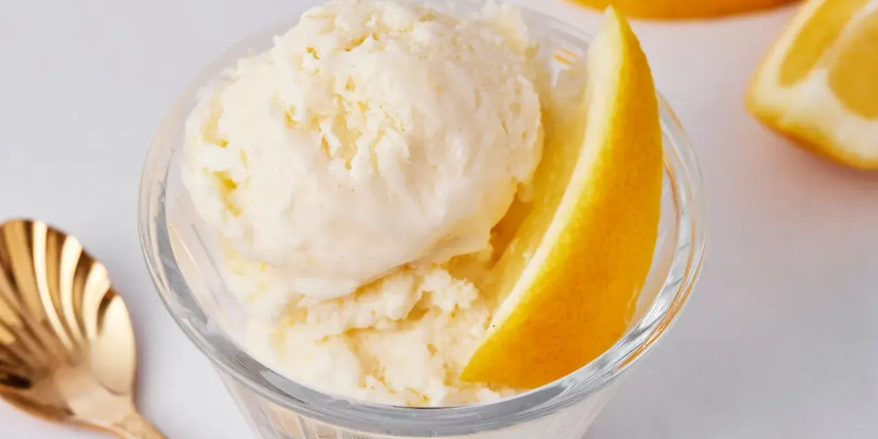 Erfrischendes Zitroneneis selber machen: Cremiges Eis im Glas mit Zitronenspalte und goldener Löffel.