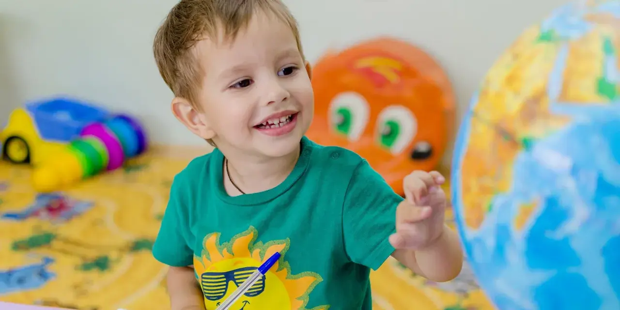 Uśmiechnięte polskie dziecko w hiszpańskiej szkole bawi się globusem i rysuje w zeszycie.