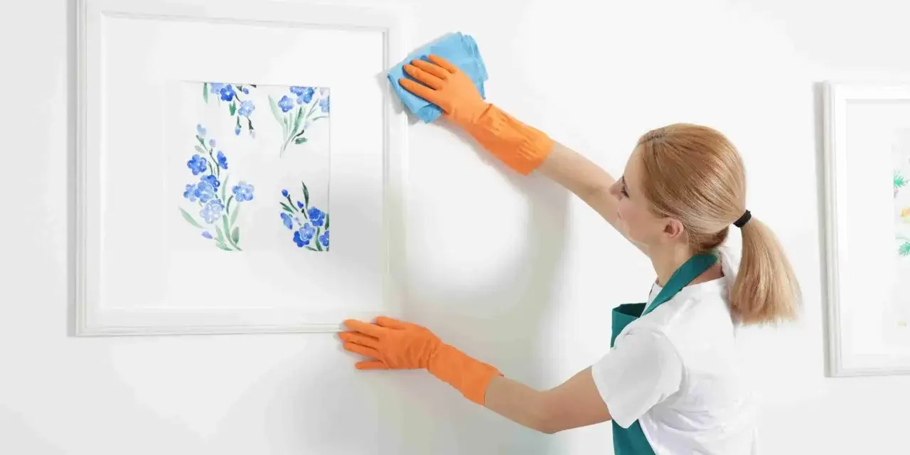 Une femme en gants orange nettoie le cadre d'un tableau de fleurs bleues. Quel produit pour nettoyer un tableau peint à l'huile ?