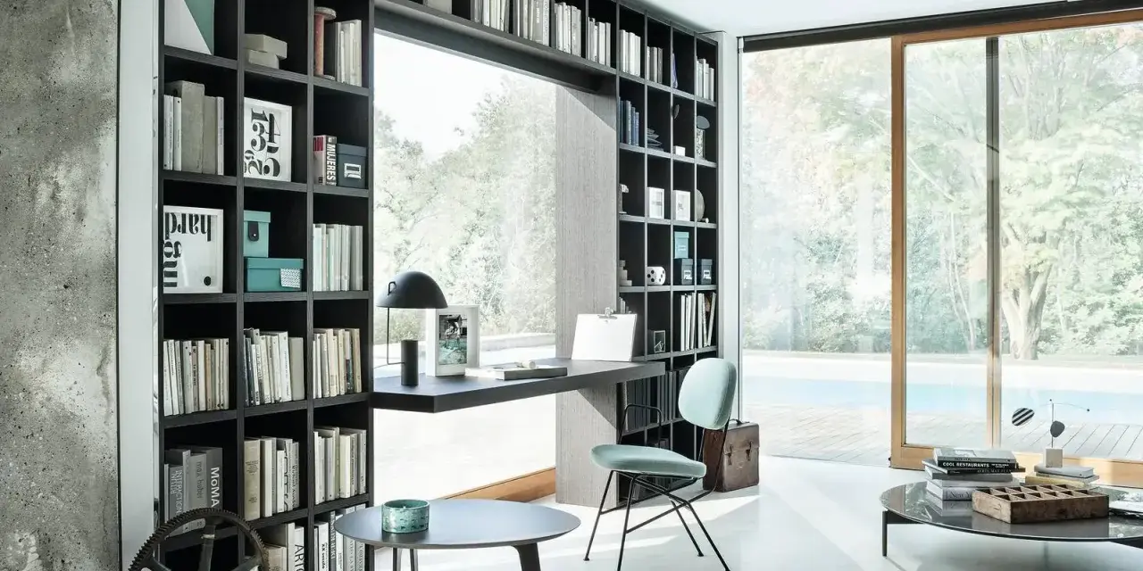 Libreria a muro con scrivania integrata, perfetta per idee stanza studio piccola. Sedia azzurra, tavolini neri e vista piscina.