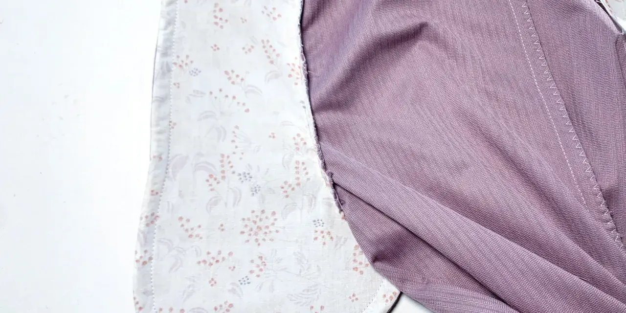 Détail d'un vêtement en cours de confection, montrant la doublure à motifs floraux des poches italiennes et le tissu extérieur violet.