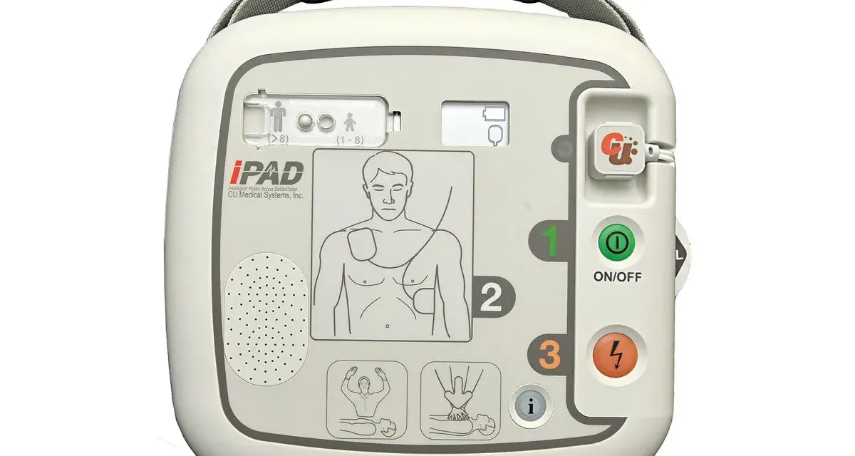 Automatyczny defibrylator zewnętrzny (AED) iPAD w kolorze białym, z widocznymi przyciskami i instrukcjami.