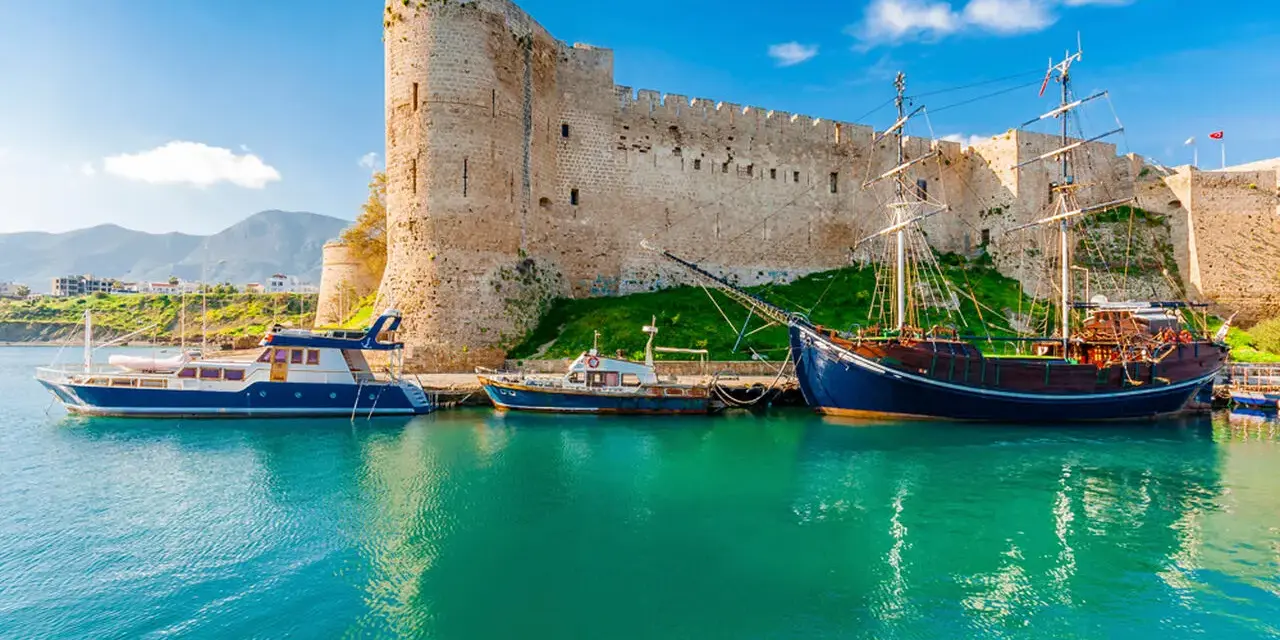 Zamek Kyrenia na Cyprze Północnym z łodziami przycumowanymi w turkusowej zatoce.