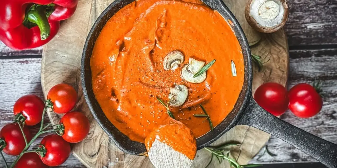 Cremige Metaxa-Sauce in einer Gusseisenpfanne, garniert mit Pilzen und Rosmarin. Daneben rote Paprika und Kirschtomaten.