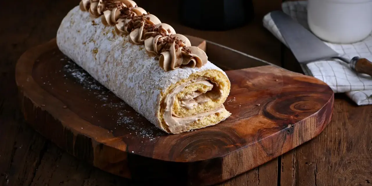 Un delicioso brazo de gitano cubierto de azúcar glas y decorado con crema de café y virutas de chocolate, listo para ser servido.