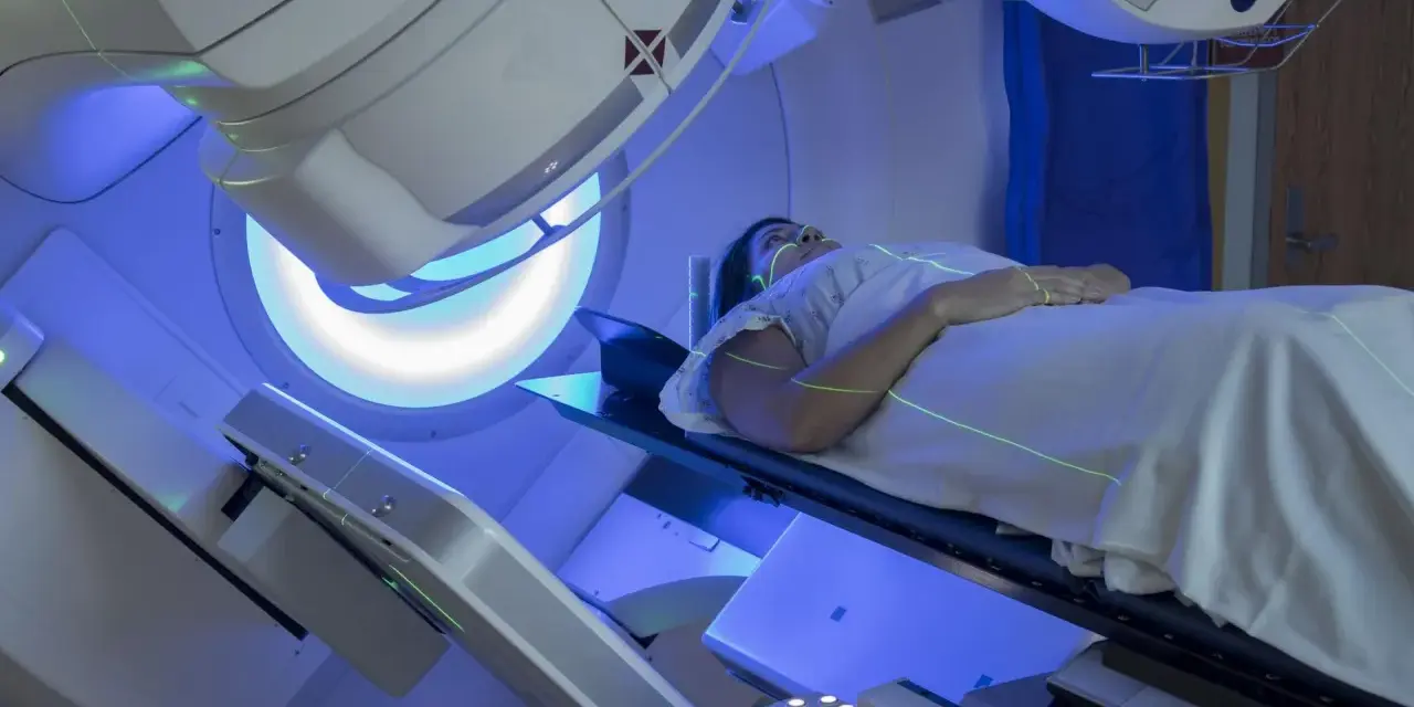 Pacjentka leży na stole zabiegowym pod aparatem do radioterapii, na jej ciele widoczne są zielone linie naprowadzające.